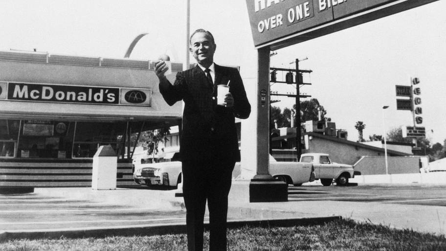 Founder and chairman of McDonald's Corporation, Ray Kroc, stands outside one of his franchises, holding a hamburger and a dri