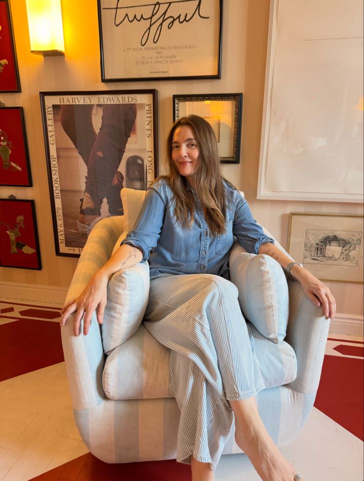 Person sitting in a chair surrounded by framed artwork on the wall