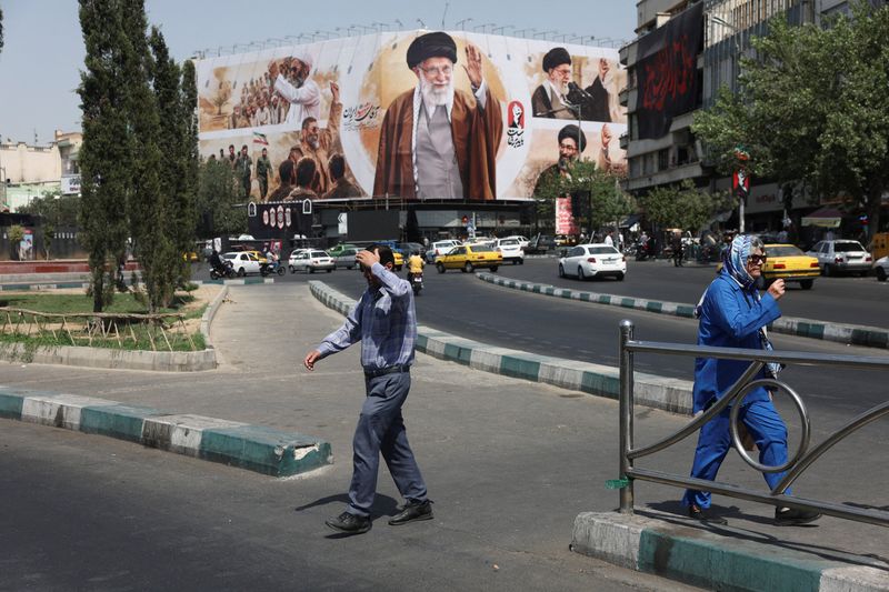 FILE PHOTO: People walk past a billboard featuring images of Iran's late Supreme Leader Ayatollah Ali Khamenei in Tehran