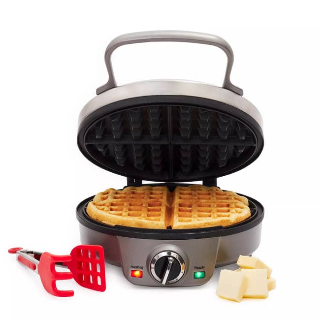 Waffle maker with a cooked waffle inside, a red spatula, and butter cubes on the side