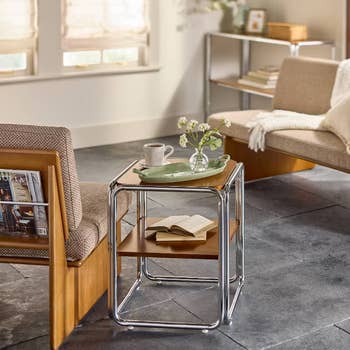 Modern living room with a nested side table holding a cup and book. Minimalist shelves and cushioned seating create a cozy reading nook