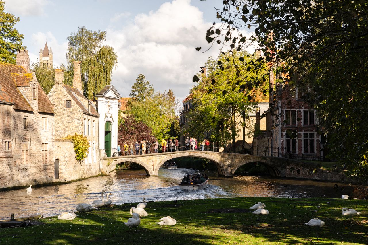 Historic stone bridge over a canal in Bruges with swans by the water and people walking across the bridge