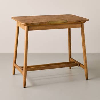 Wooden writing desk with a minimalist design and tapered legs, featuring a small drawer with a brass pull. Perfect for home office use