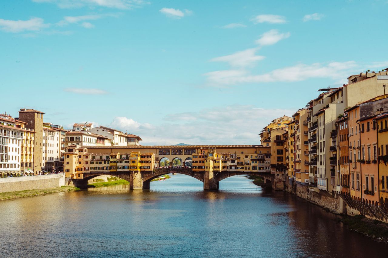 The Ponte Vecchio bridge over the Arno River with buildings lining the riverbanks in Florence Italy