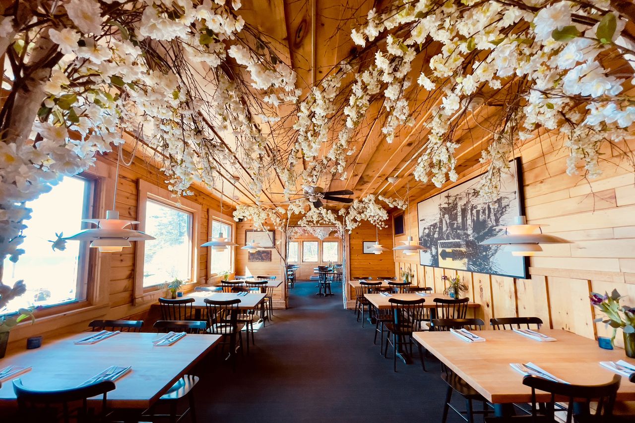 Interior of a rustic cafe with wooden walls and tables ceiling decorated with hanging flowers large framed photo on the wall and natural light entering