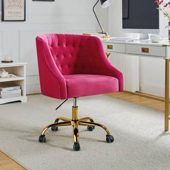 Pink velvet swivel office chair with tufted backrest on gold wheels in a modern home office setting
