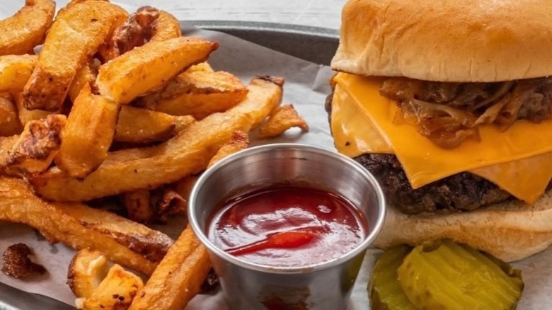 Cheeseburger on tray with fries, ketchup, and sliced pickles