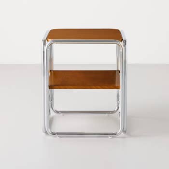 A modern, minimalist side table with chrome legs and two wooden shelves, suitable for contemporary home decor