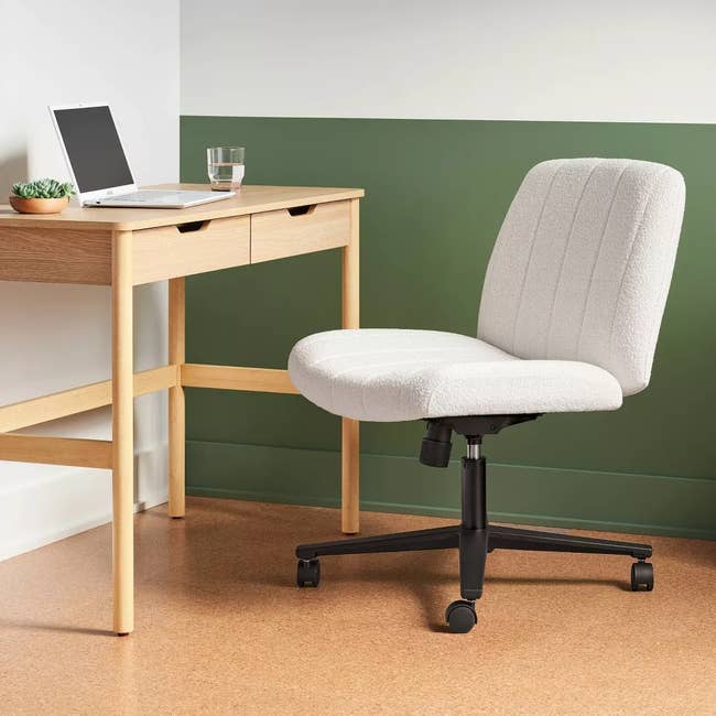 Home office with a wooden desk, laptop, glass of water, and plush office chair with wheels