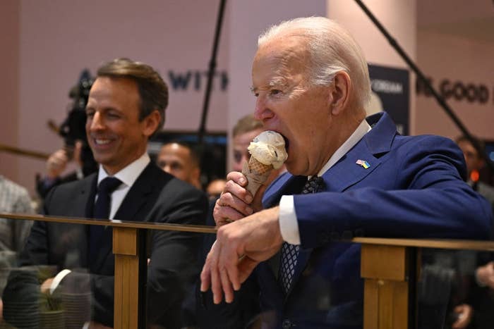 A person in a suit enjoys an ice cream cone at a public event while others look on smiling