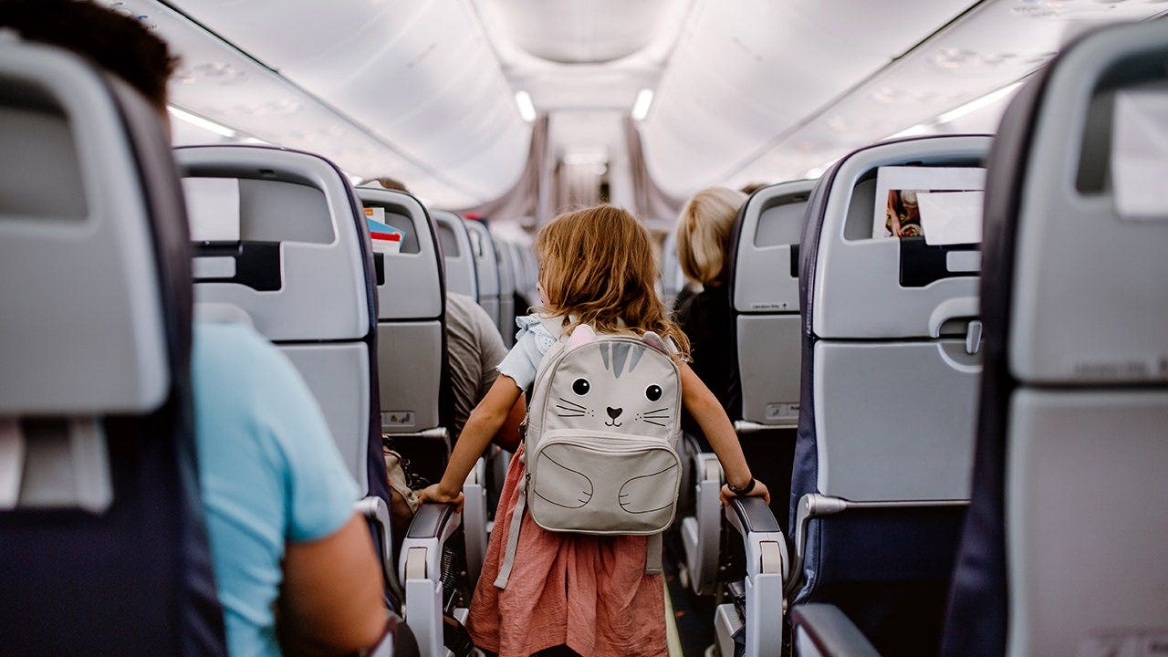 Little girl with backpack stands in the airplane aisle.