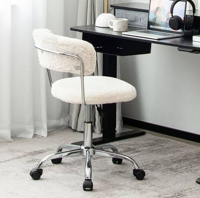 Desk with a white swivel chair, headphones, coffee mug, and lamp near a curtain, creating a cozy, minimalist workspace