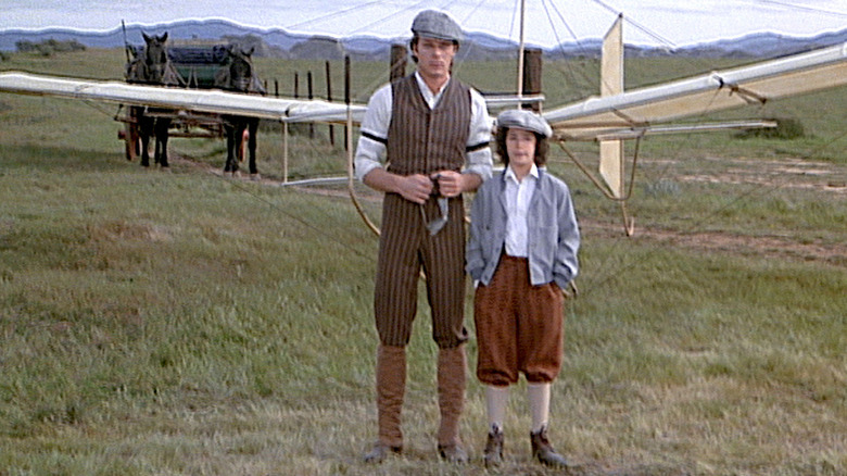 A man and a young boy standing in a field in front of early airplane
