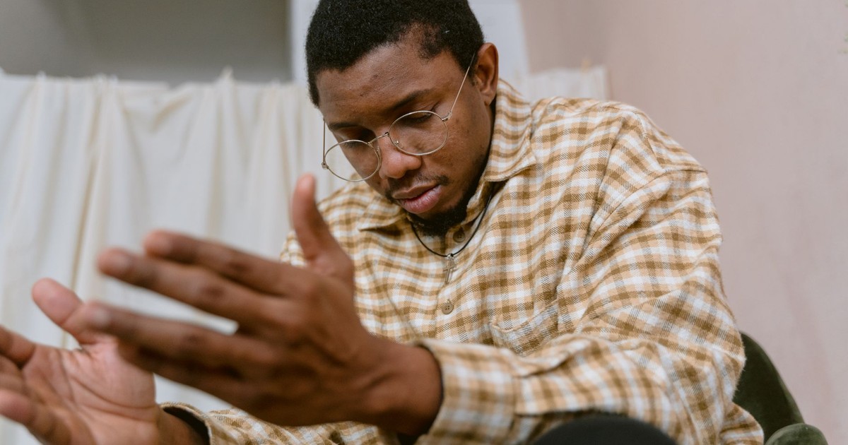 Close-up of a man wearing glasses and plaid shirt, appearing reflective indoors.