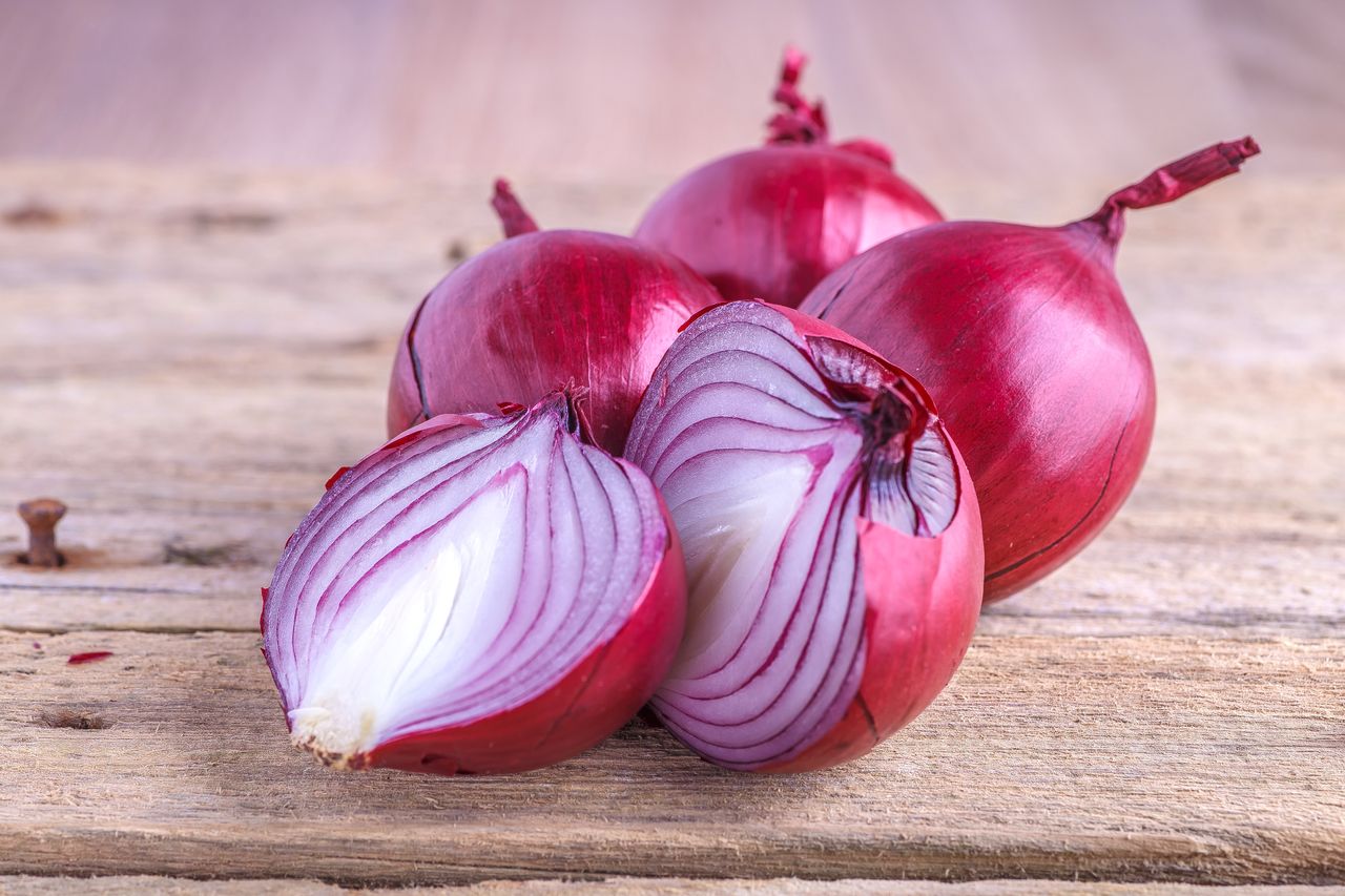 Four whole red onions and one halved on a wooden surface