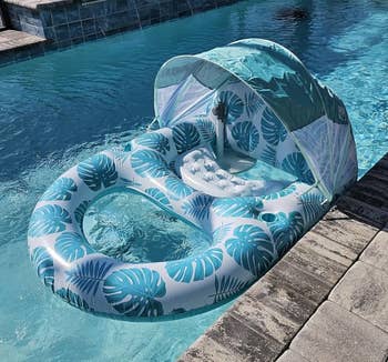 Inflatable pool float with canopy and leaf pattern floats in a backyard pool beside a stone deck