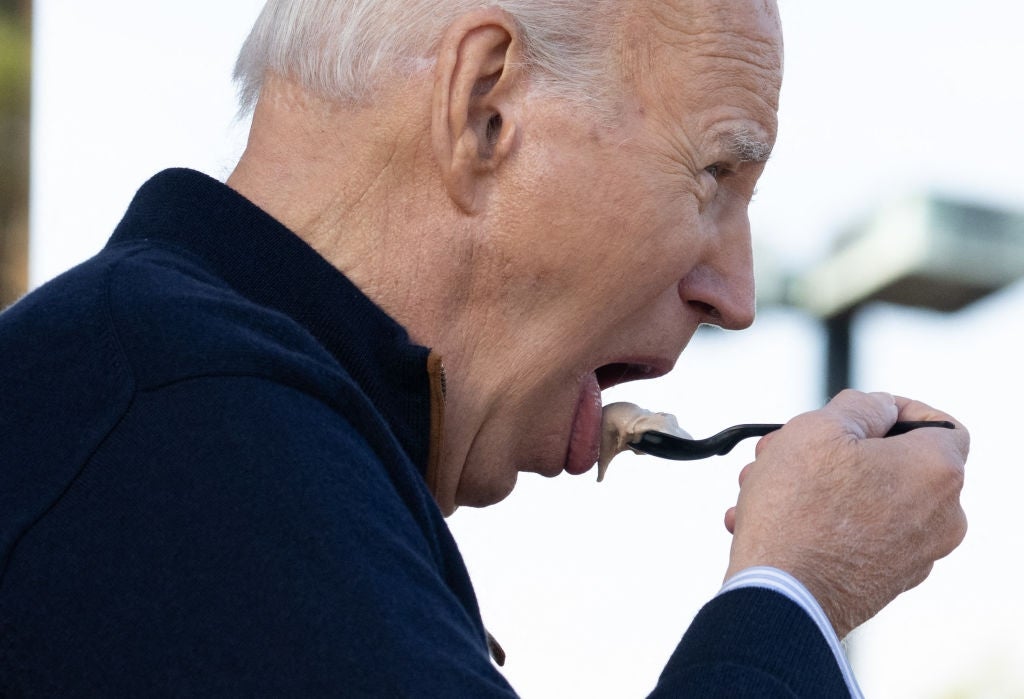 A man eats ice cream from a spoon, wearing a dark jacket with a relaxed expression
