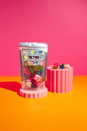 Retro bath pearls in a clear bag on a pink podium, displayed amidst a bright setup. Perfect for adding a colorful touch to bath time