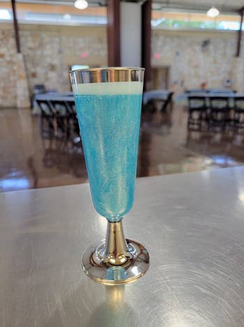 A sparkling blue drink in a champagne flute on a metal table in a banquet room setup