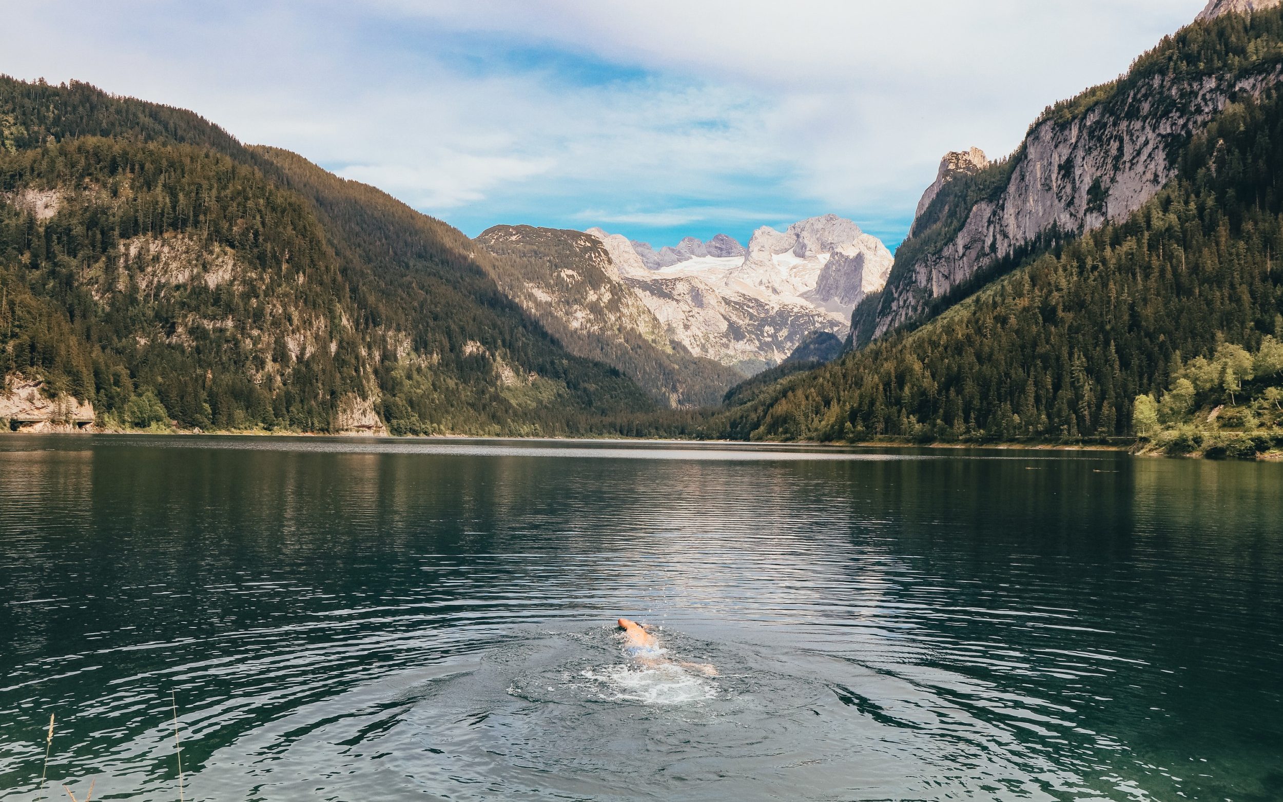 man swims in a glacial lake Gosausee overlooking the Austrian Alps