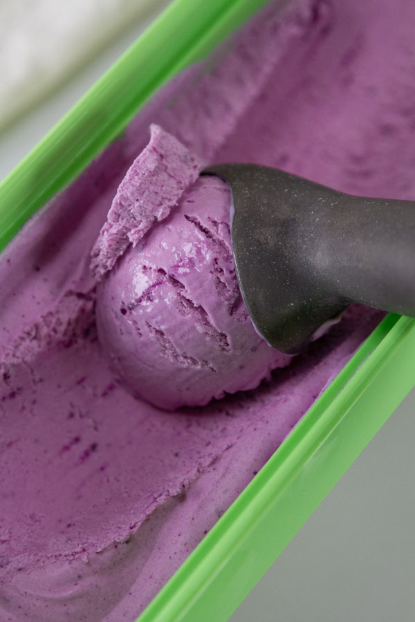 scooping out ube ice cream from a green ice cream container.