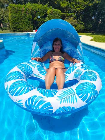 Person relaxing in a leaf-patterned inflatable pool float with a canopy