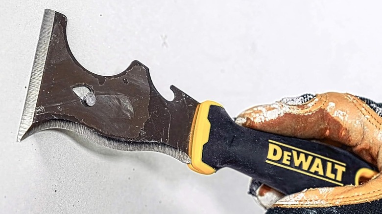 A person using paint scraper tool on wall
