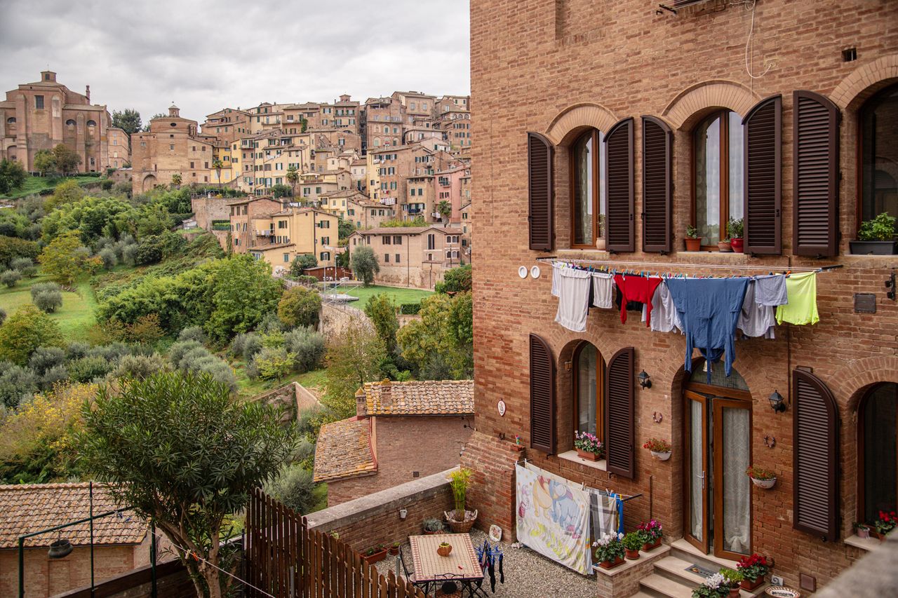 A cityscape with old buildings a residential scene in the foreground with clothes hanging to dry outside windows and a hillside view