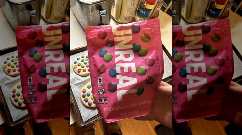 Hand holding bag of Unreal milk chocolate gems in front of cookies