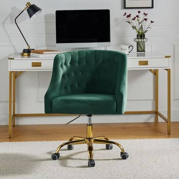 Elegant workspace with a tufted swivel chair, gold legs, a white desk, computer, lamp, and flowers, set on a wooden floor with a rug