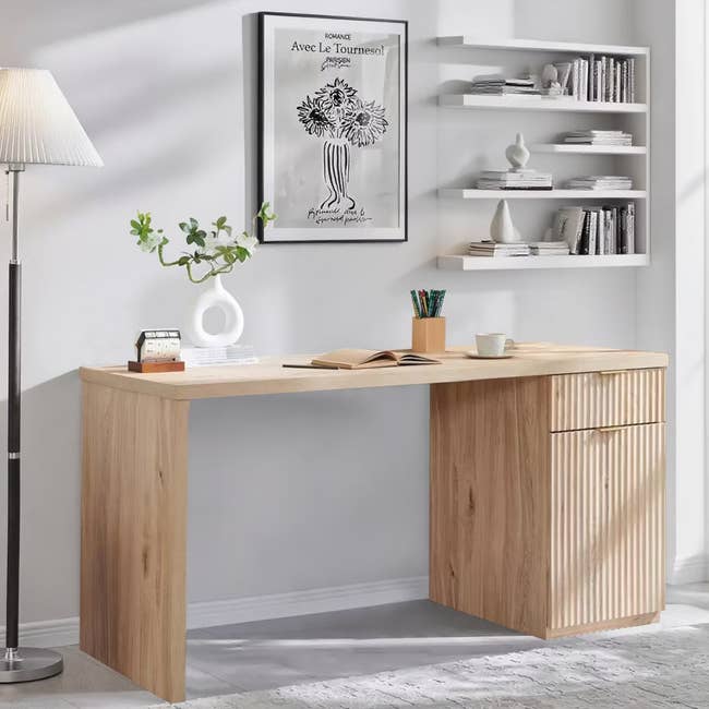 Sleek wooden desk in a modern room with a potted plant, books, and minimalist wall decor. Shelves hold books and decorative items