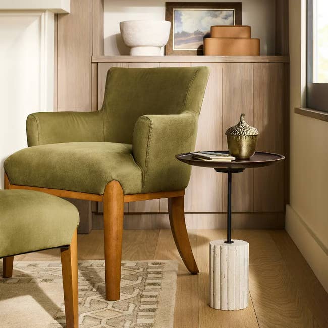 Stylish green armchair with wooden legs next to a side table, featuring decorative items in a cozy, modern living room setting
