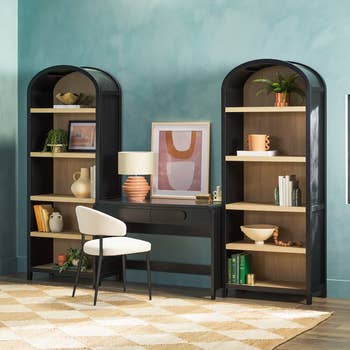 Home office setup with a sleek black desk, modern chair, and two arch bookshelves decorated with books and decor items