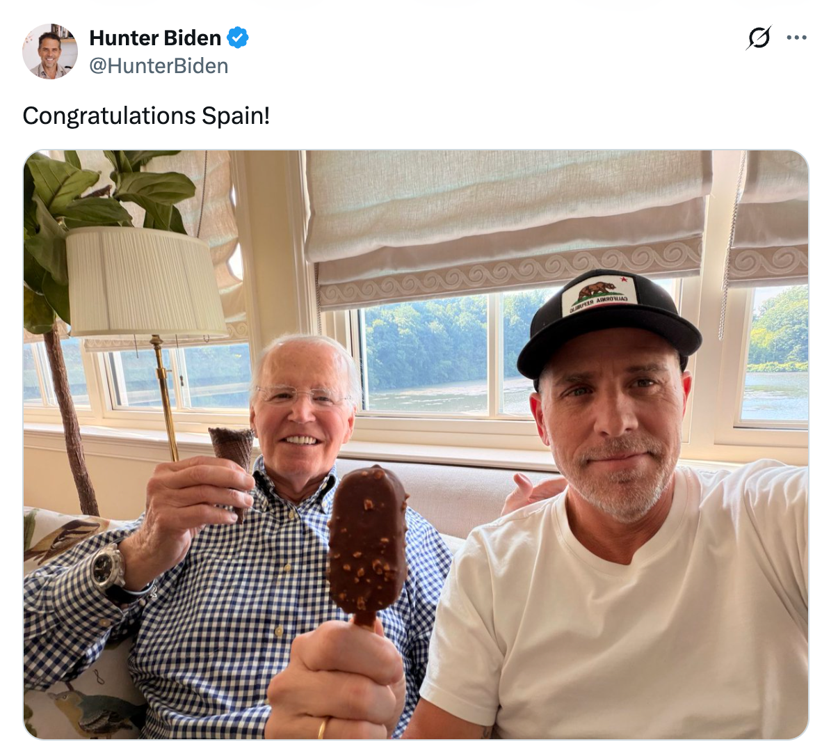 Two people smiling, holding ice cream bars indoors. One wearing a button-up shirt, the other a cap and t-shirt. Tweet text: "Congratulations Spain!"