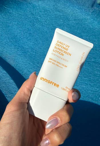 Person holding Innisfree Daily UV Defense Sunscreen Lotion by a pool