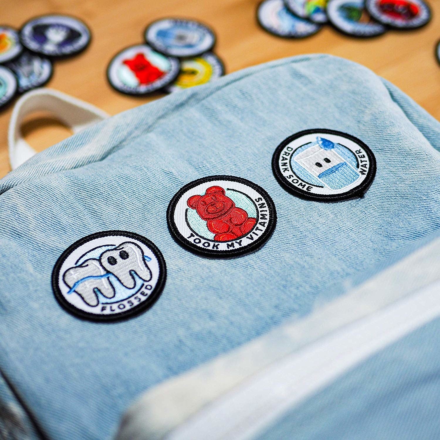 Denim backpack with round patches: a tooth with "Flossed," a gummy bear with "Took My Vitamins," and a water bottle with "drank some water"
