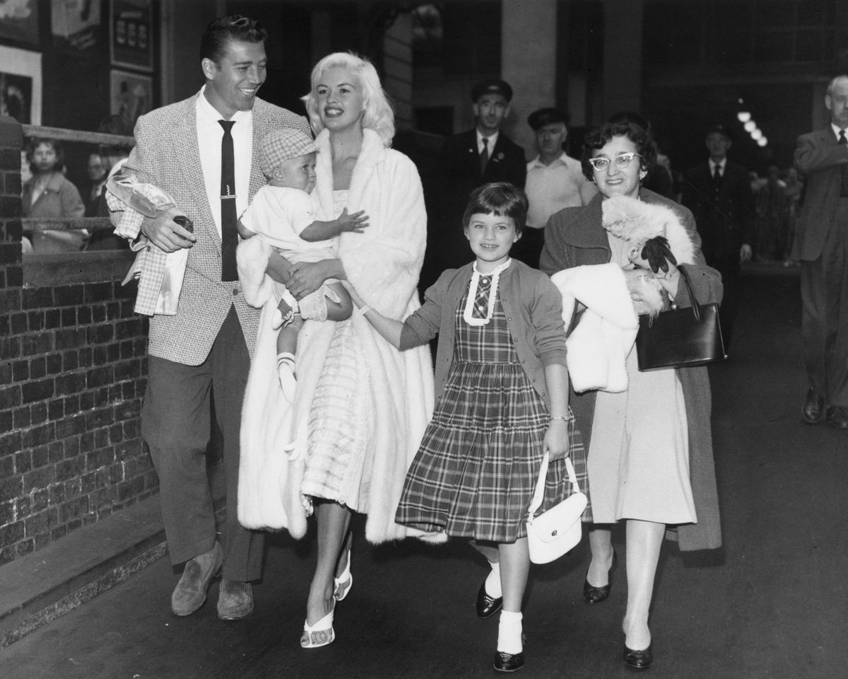 Jayne Mansfield walking with a group of people holding a baby in her arms