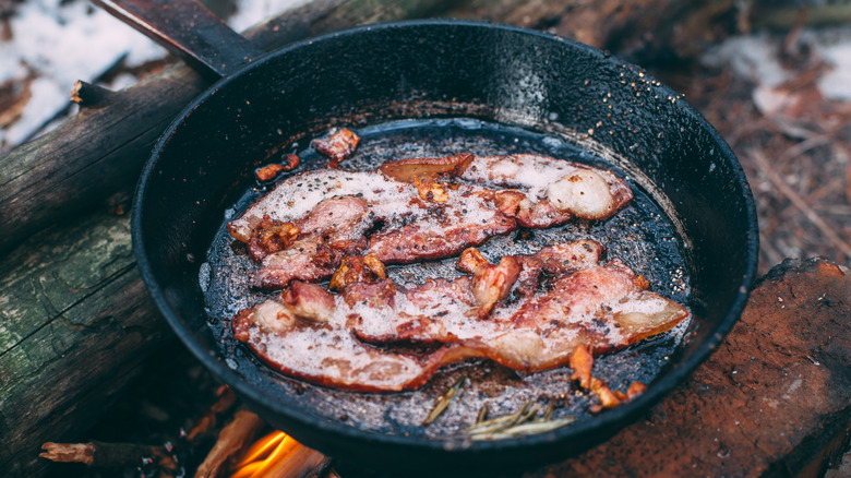 Bacon cooking in a skillet over a fire