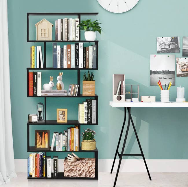 Modern home office with a sleek black bookshelf filled with books, plants, and decorative items, next to a minimalist white desk