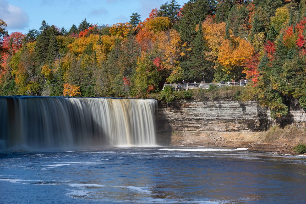 A wide cascading waterfall surrounded by a forest with autumn foliage Tahquamenon Falls in Michigan