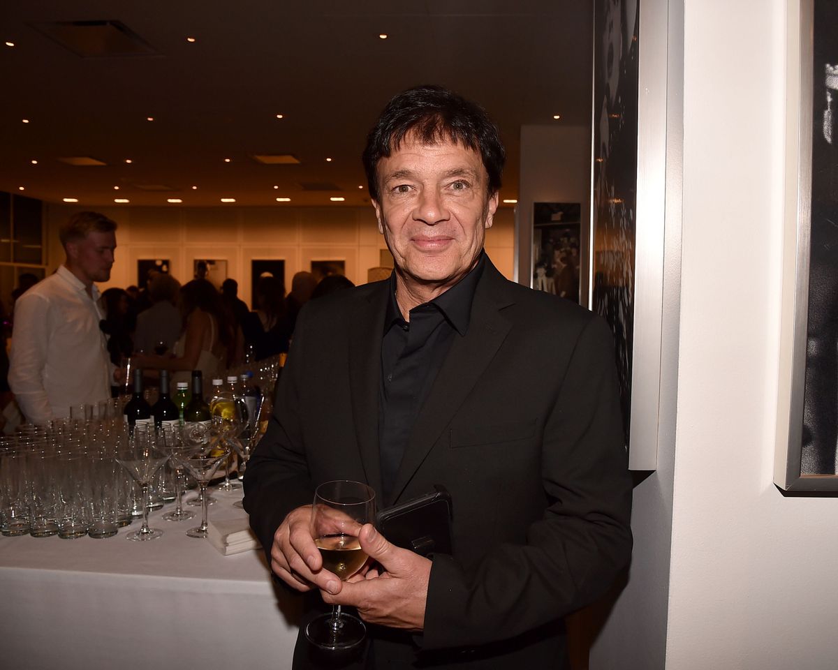A man holding a glass stands near a table in an indoor event space