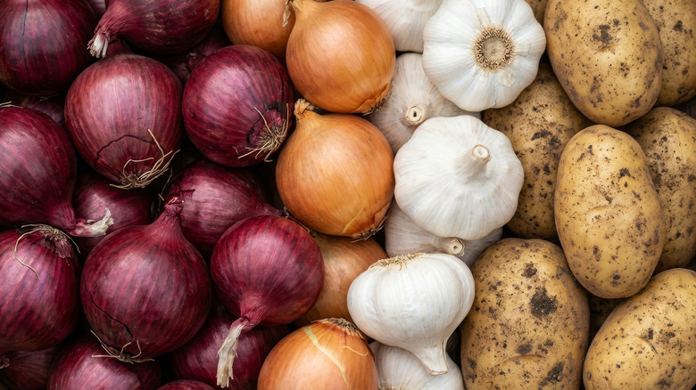 A pile of red and yellow onions, garlic, and potatoes