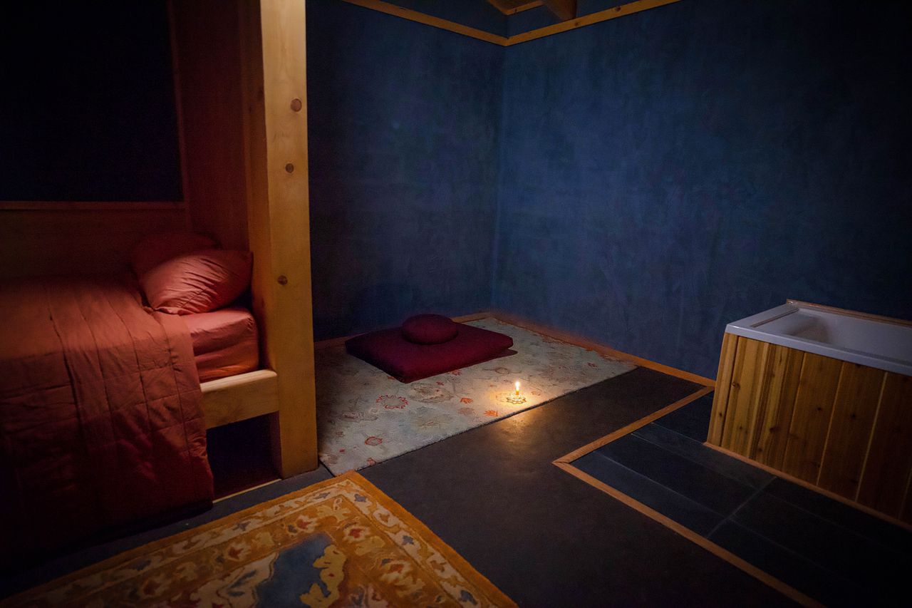 A dimly lit interior of a retreat cottage featuring a bed meditation mat candlelight and wooden features