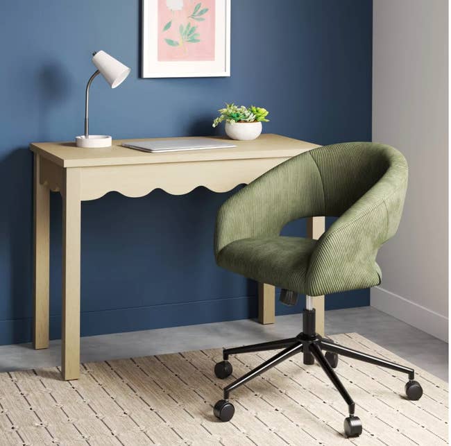 Modern home office with beige desk, task lamp, and green swivel chair on wheels. Neutral decor promotes a minimalist shopping aesthetic