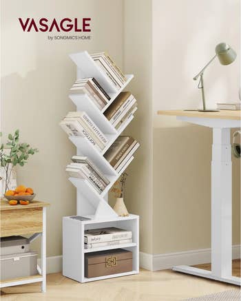 Vasagle tree-shaped bookshelf in a modern room, holding books and decor, near a desk with a lamp