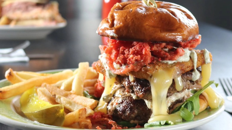 Cheeseburger with onion strings, block of pepperjack, and pickle on plate with fries