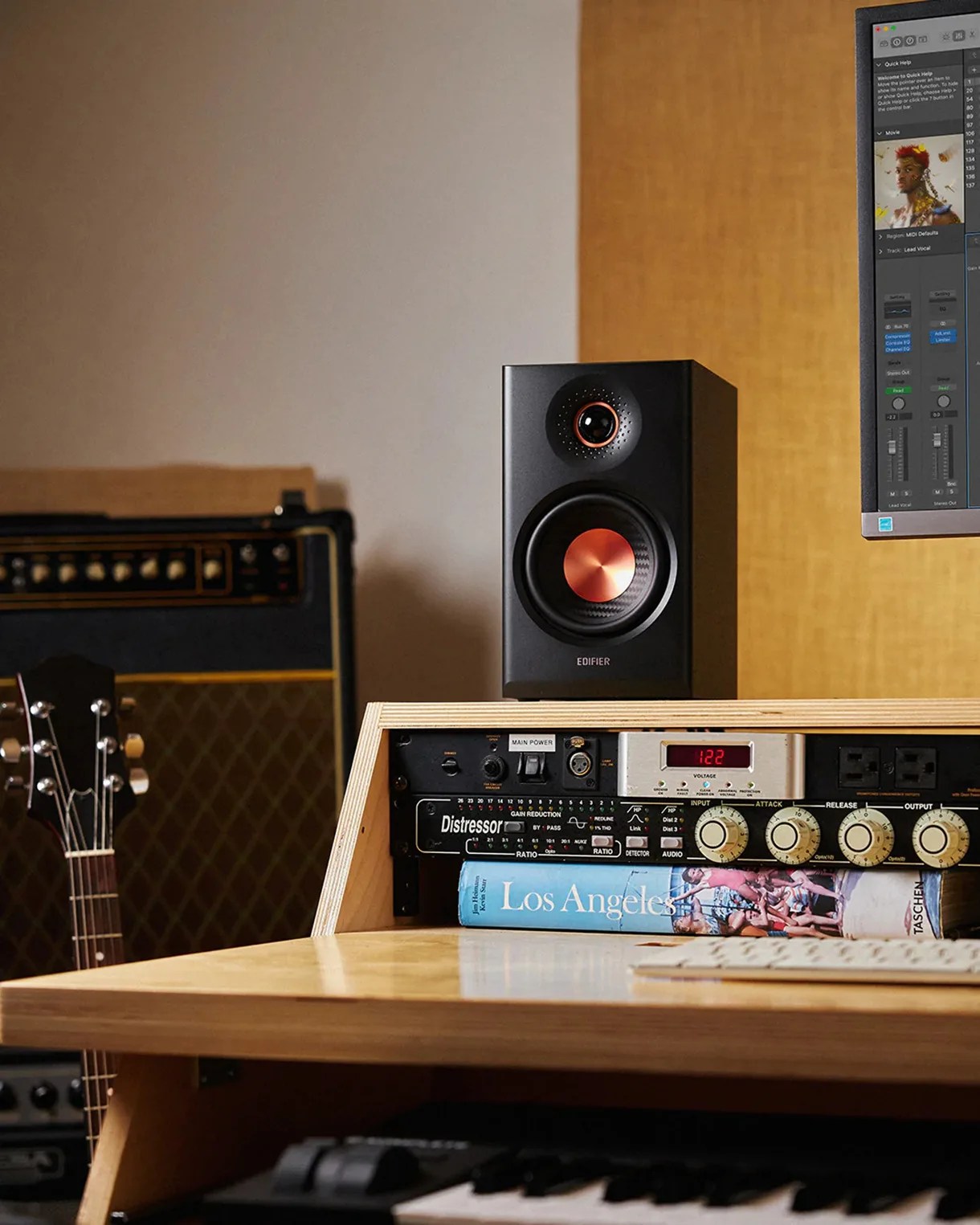 Black Edifier speaker with copper-colored speaker cones on a wooden desk near audio equipment and a guitar.