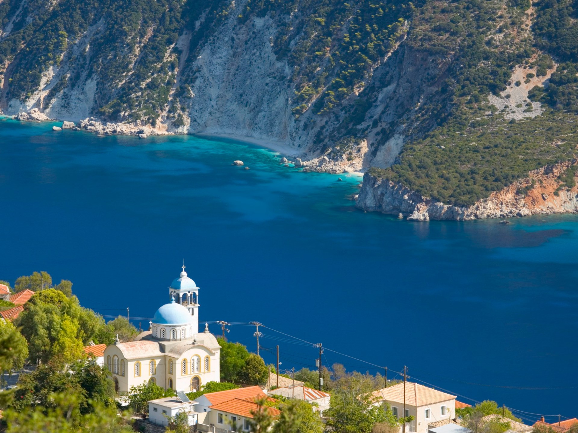 Village houses and church precariously perched above the deep blue waters of Afales Bay, Exogi, Ithaca.