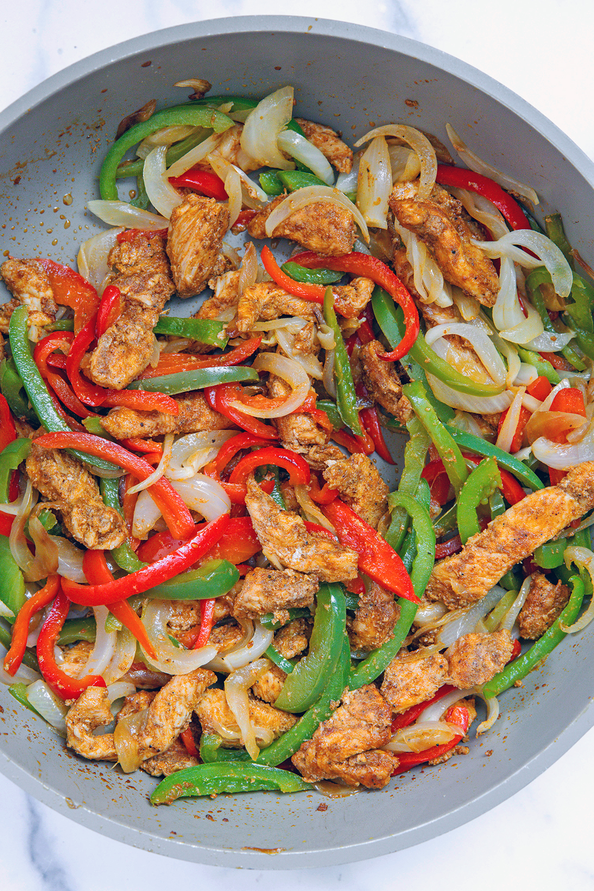 Chicken, peppers, and onions cooking in a skillet.