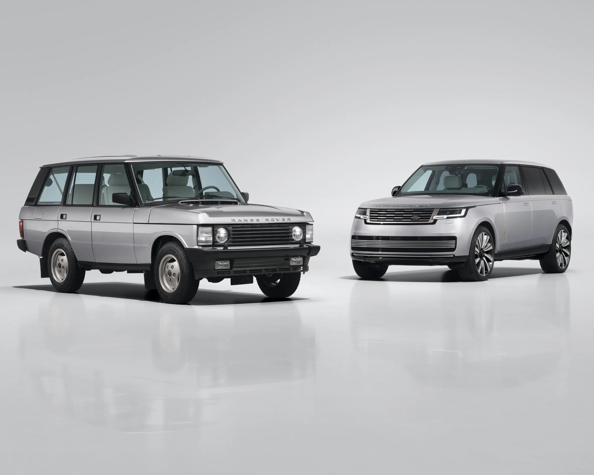 Two silver Range Rover SUVs, one classic model on the left and a modern model on the right, on a white reflective floor.